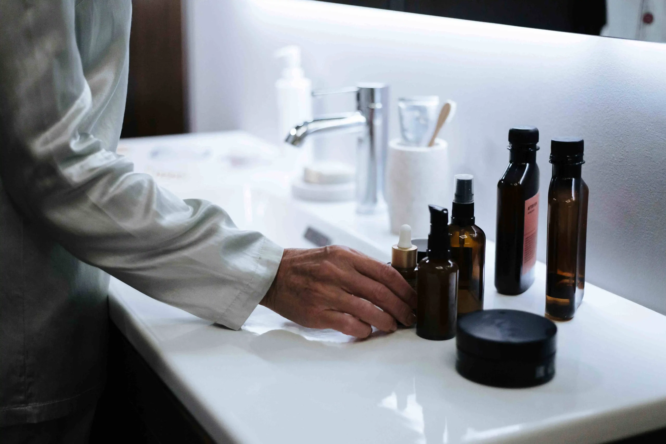 Hand selecting skincare products on a bathroom counter, illustrating seasonal skincare tips for adjusting a routine year-round