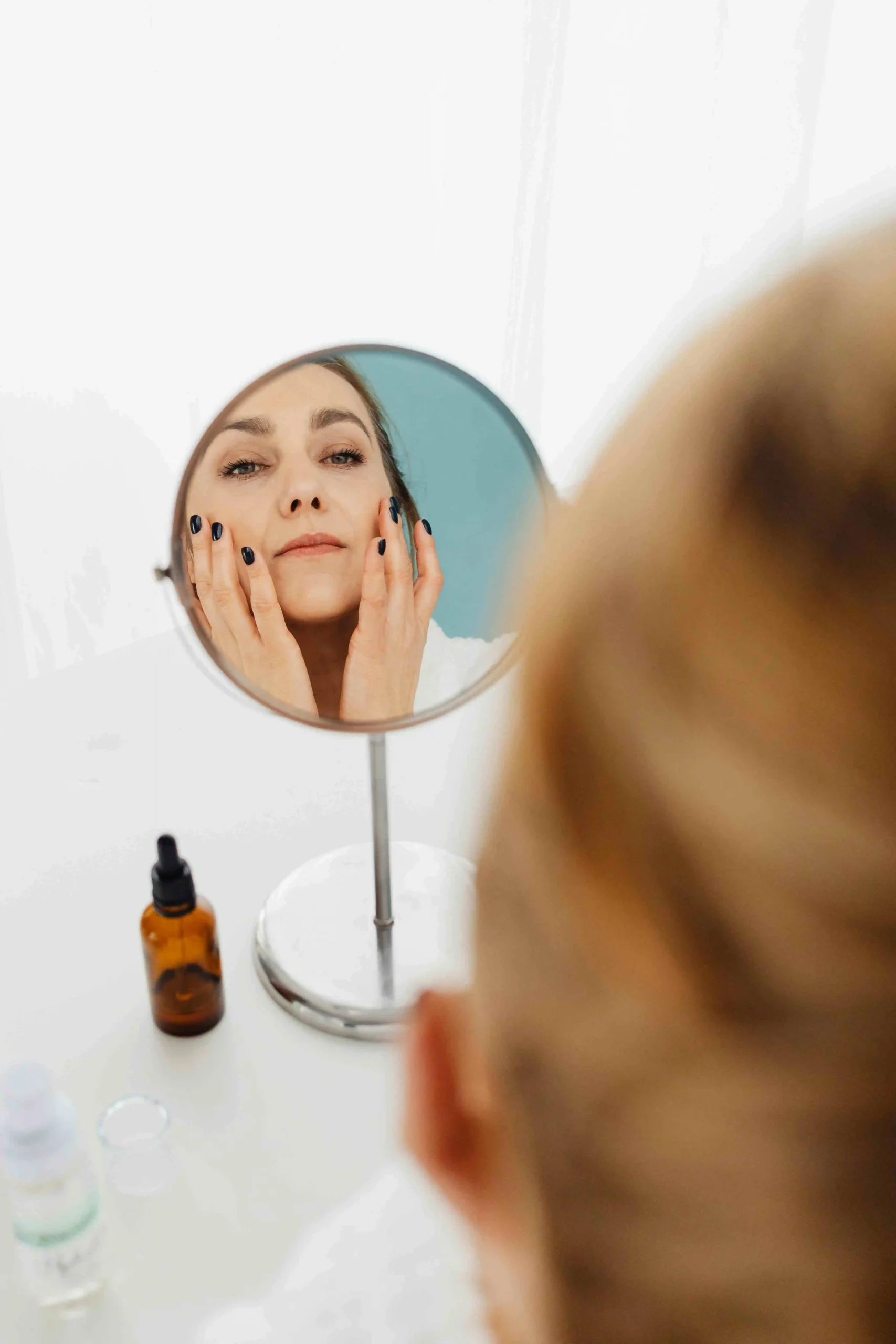Person applying skincare products in front of a mirror, demonstrating proper skincare layering technique