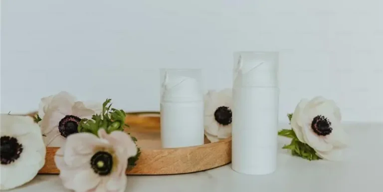 Minimalist white skincare containers displayed with flowers, symbolizing eco-friendly skincare packaging