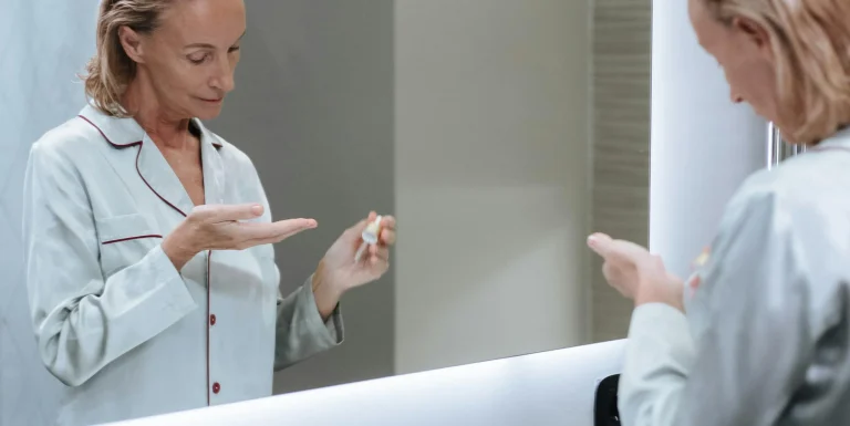Person examining a skincare product in front of a mirror, highlighting
