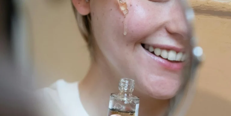 Person applying face serum while following a simple skincare routine in front of a mirror