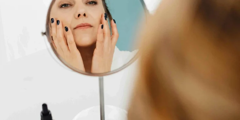Person applying skincare products in front of a mirror, demonstrating proper skincare layering technique